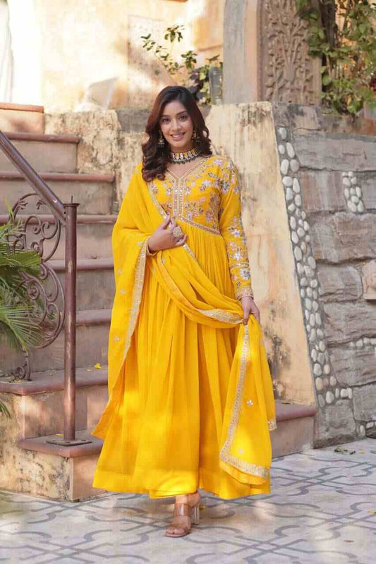 Woman in a yellow traditional outfit standing outdoors with stone steps and plants in the background