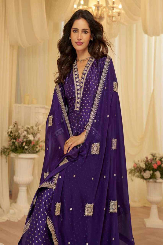 Woman in a purple traditional outfit with intricate designs in a decorated indoor setting.