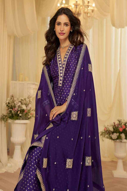 Woman in a purple traditional outfit with intricate designs in a decorated indoor setting.